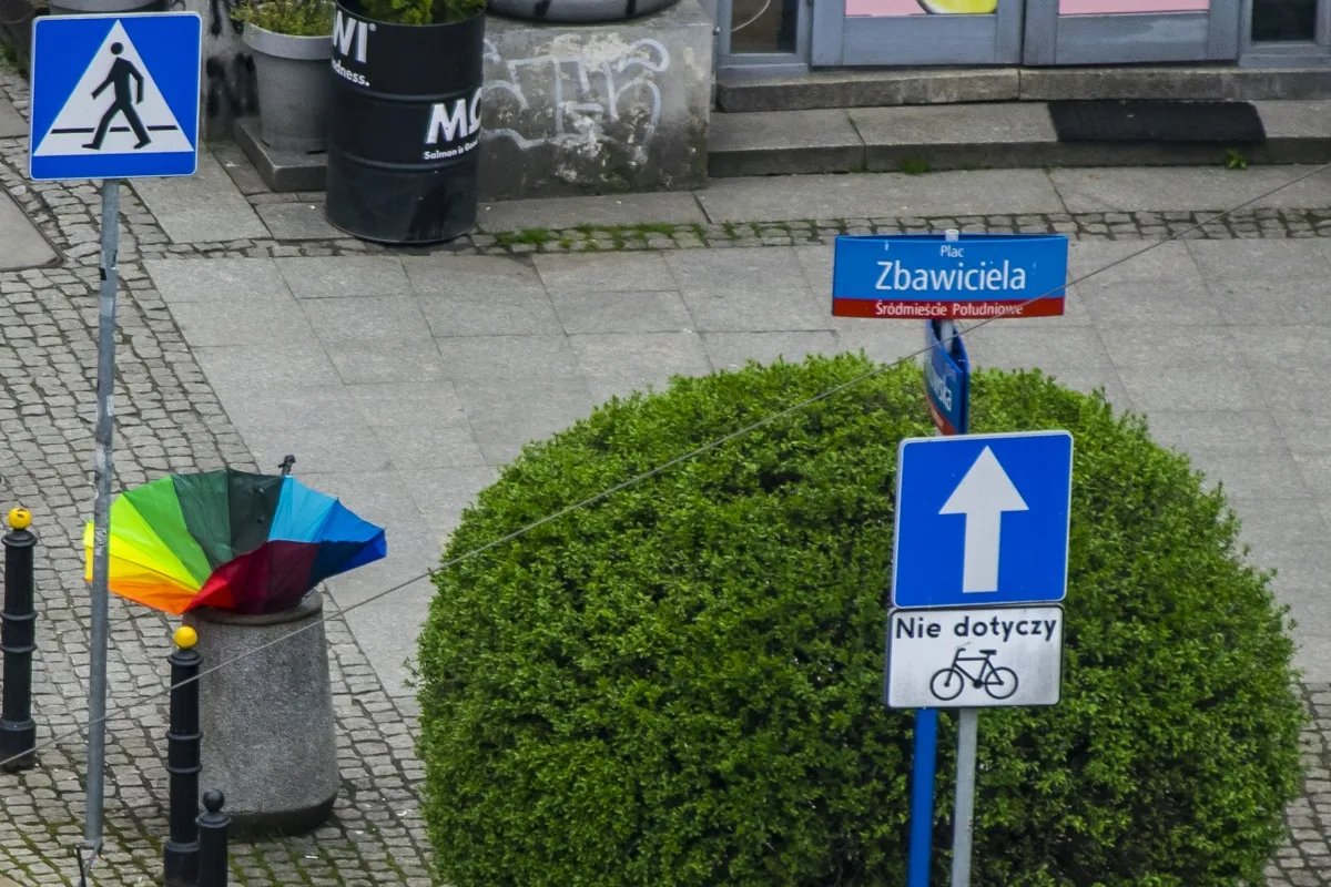 Rainbow umbrella resting in a street bin beside traffic signs